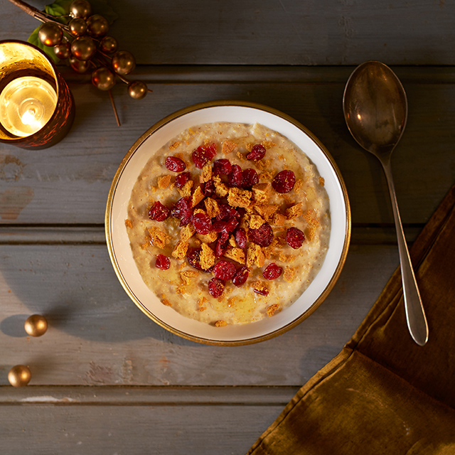 bowl full of gingerbread porridge topped with cranberries, crushed biscuits and honey