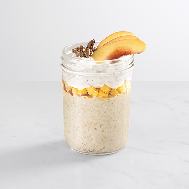 chia peach overnight oats topped with pecans and peach slices in a glass