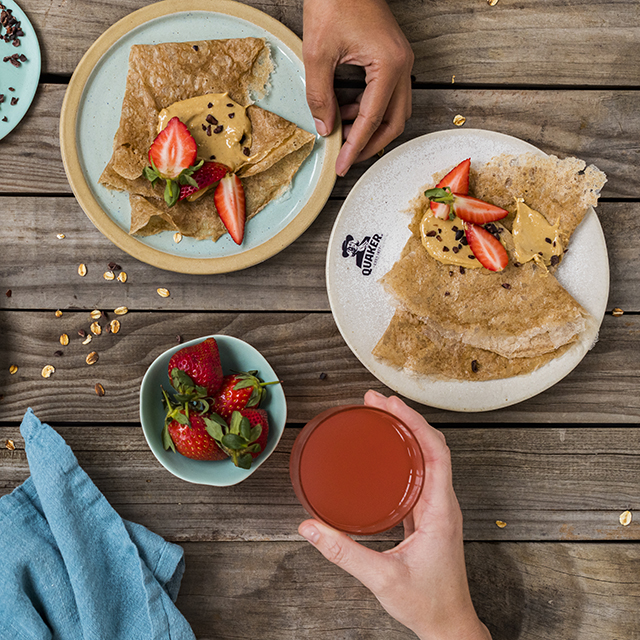 strawberry, cashew butter and cacao nibs crepes on a plate with slices of strawberry and a glass of juice